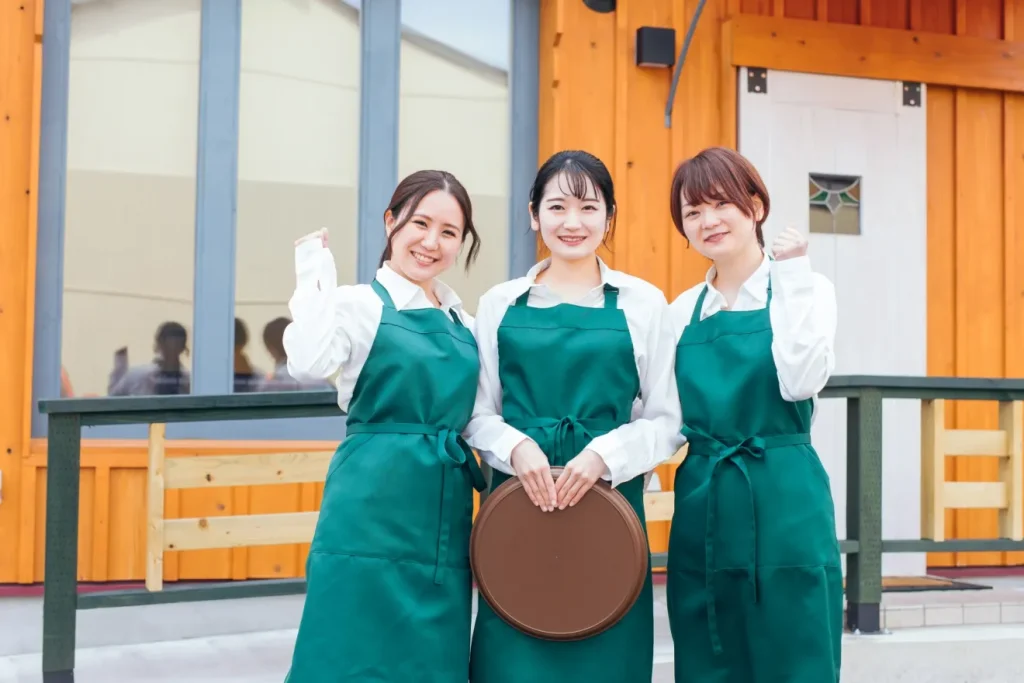 カフェ店の前でガッツポーズする3人の女性店員