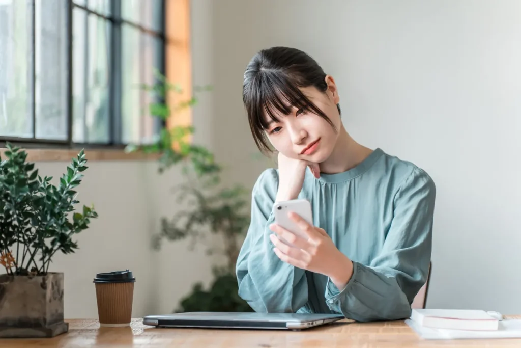スマートフォンで求人サイトを見て首を傾げる女性